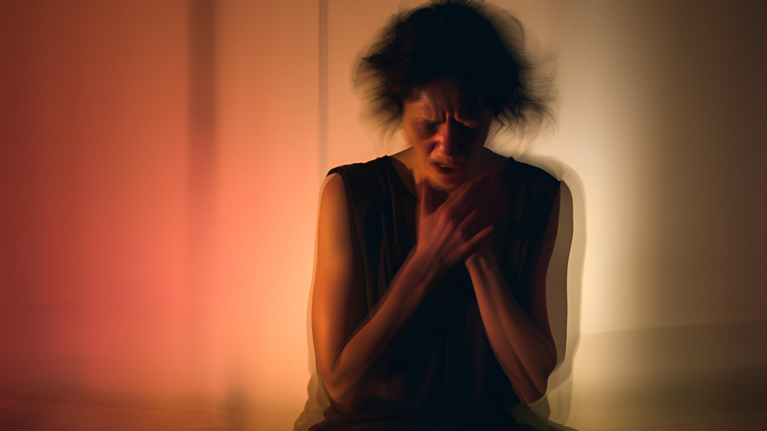 Woman in visible distress clutching her hands to her chest in a dimly lit room