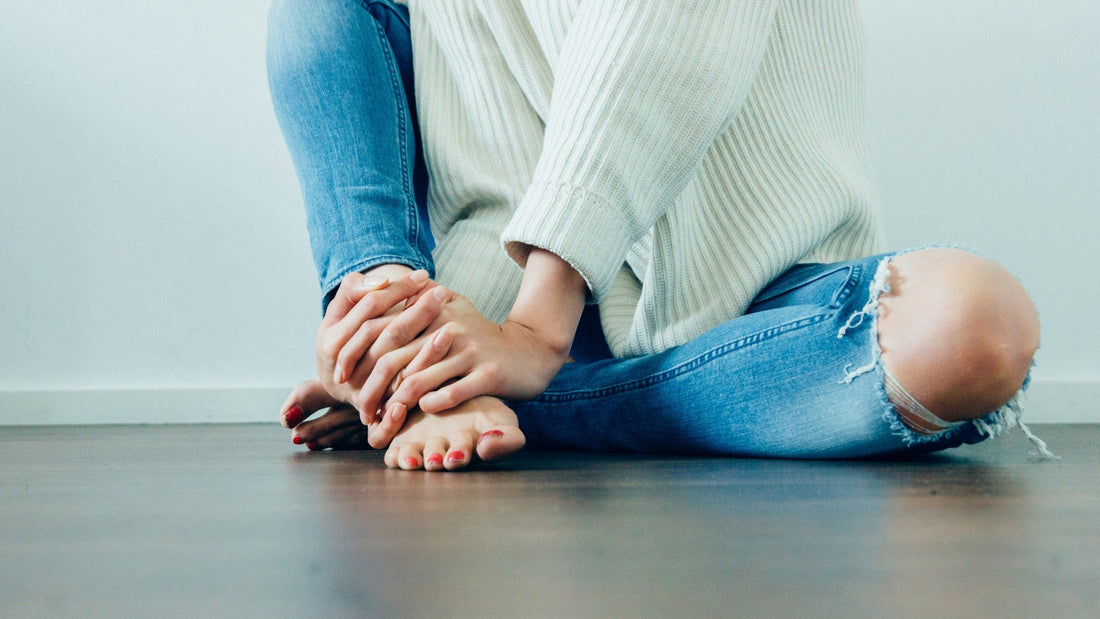 Person sitting on the floor holding a sore ankle with both hands.