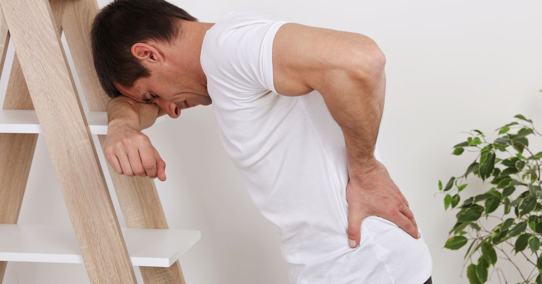Man leaning on a wooden ladder and holding his lower back in pain