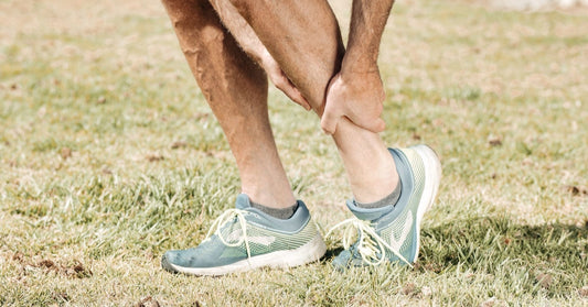 Runner on grass gripping the back of his lower leg after a calf muscle strain