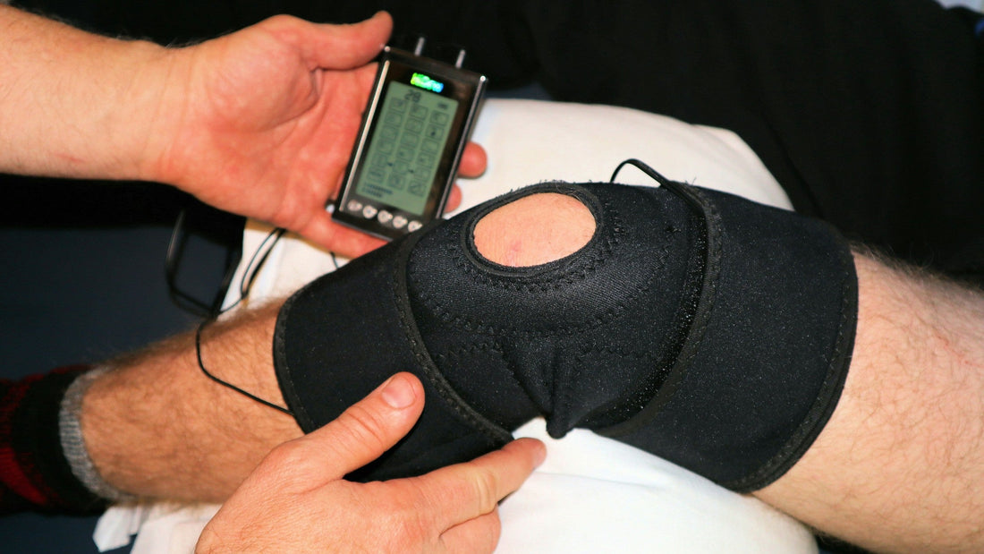 Person holding a TENS unit connected to an electrode sleeve wrapped around the knee