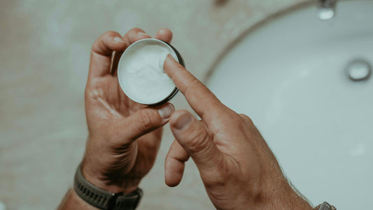 Fingertip scooping topical pain relief cream from an open jar.